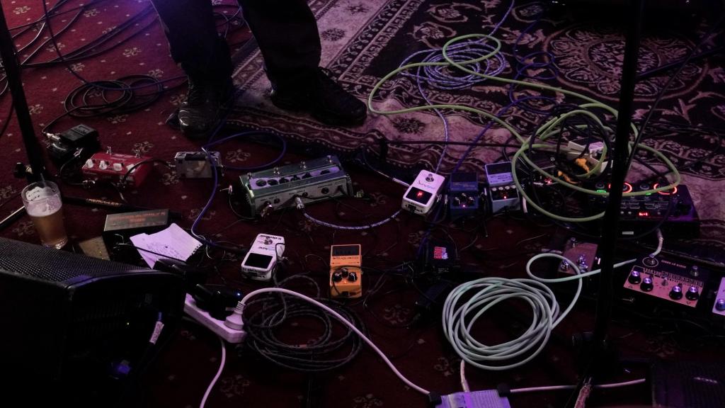 at least ten pedals and instrument cables, multiple power supplies and electricity cords littering the front of the stage.